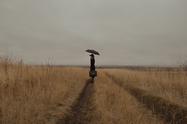 Mujer de negro con paraguas negro en un campo de hierbas secas mirando al infinito